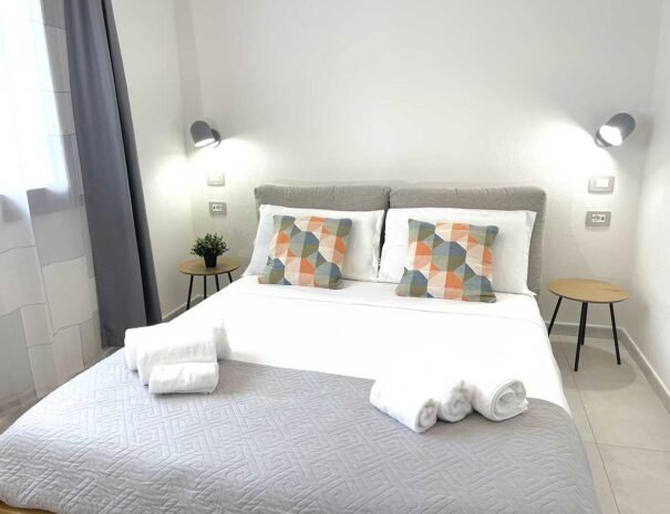 Interno luminoso della camera da letto matrimoniale dell'appartamento Domus Luna, casa vacanze a Teulada, con arredi moderni, cuscini geometrici e atmosfera accogliente