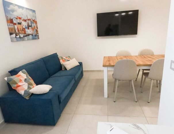 Zona relax del soggiorno di Domus Soli con comodo divano rosso e illuminazione naturale perfetta per il riposo