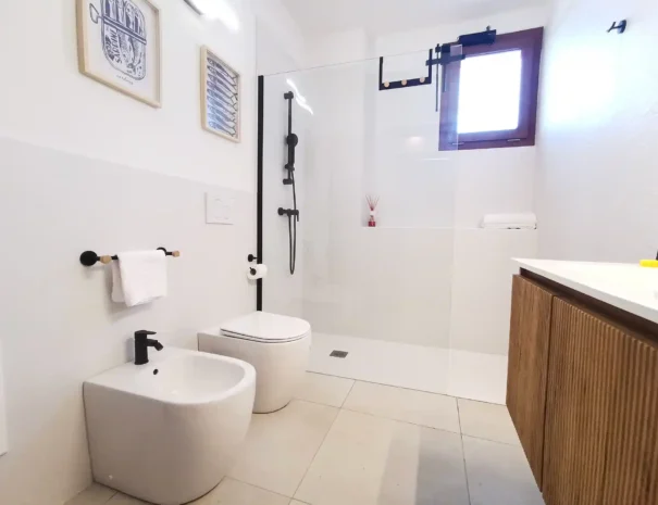 Interno del bagno moderno di Domus Luna con sanitari bianchi, bidet, WC e ampio box doccia con finiture eleganti e rivestimenti chiari.