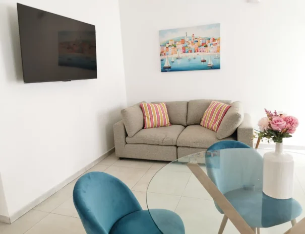 Angolo intrattenimento del soggiorno di Domus Luna con TV a schermo piatto installata a parete, poltroncine moderne azzurre e decorazioni murali.