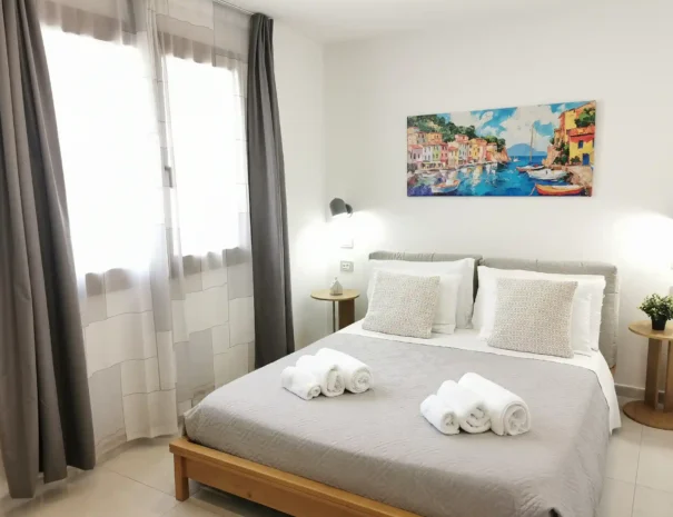 Prospettiva della camera matrimoniale di Domus Luna che mostra il letto spazioso, la finestra che garantisce luce naturale e l'arredamento minimalista moderno.