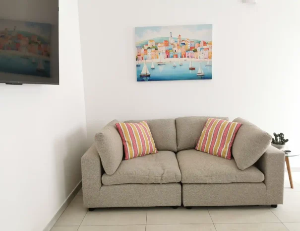 Zona giorno di Domus Luna con ampio divano beige trasformabile in letto, cuscini d'arredo arancioni e ambiente luminoso ideale per il relax.