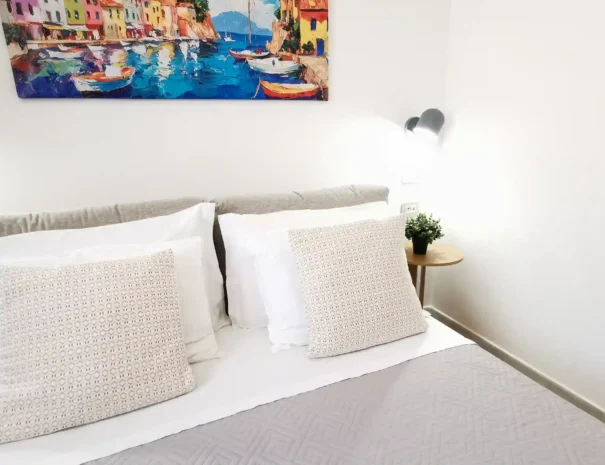 Primo piano del letto matrimoniale presso Domus Luna con cuscini bianchi soffici, testiera moderna in legno e biancheria da letto di alta qualità.