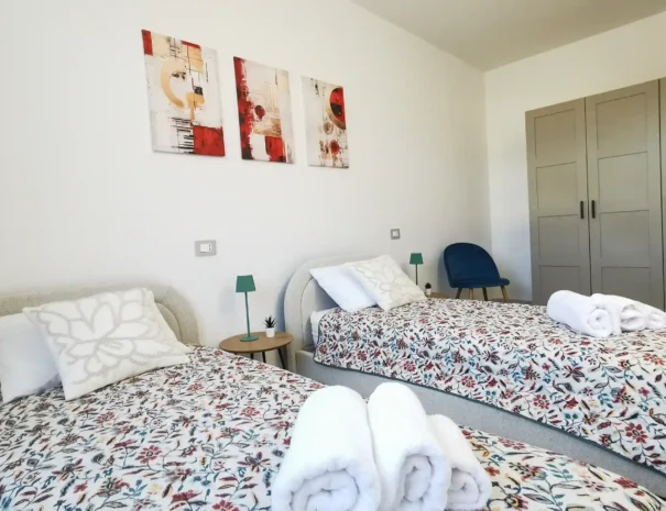 Seconda camera da letto di Domus Luna con due letti singoli, biancheria coordinata e arredi moderni, ideale per famiglie o gruppi.